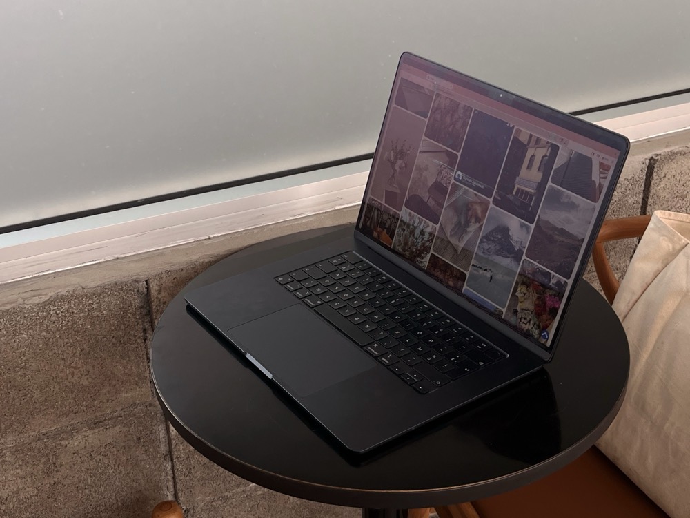 An open laptop on a small round cafe table beside timber chairs.